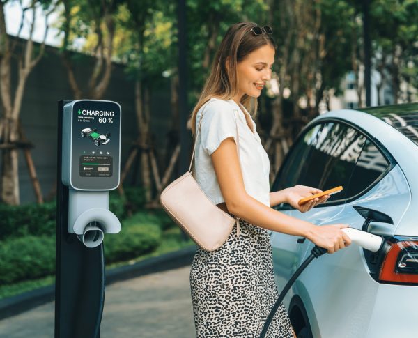 Young woman travel with EV electric car charging in green sustainable city outdoor garden in summer. Urban sustainability lifestyle by green clean rechargeable energy of electric BEV vehicle innards